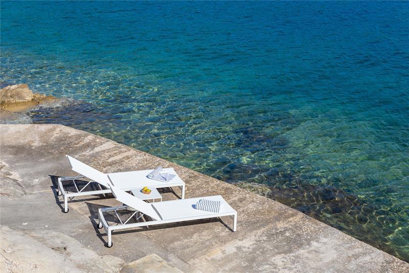 Two sun loungers side by side on a stone bathing jetty over clear water, a shared table between them, at Sumartin on Brač