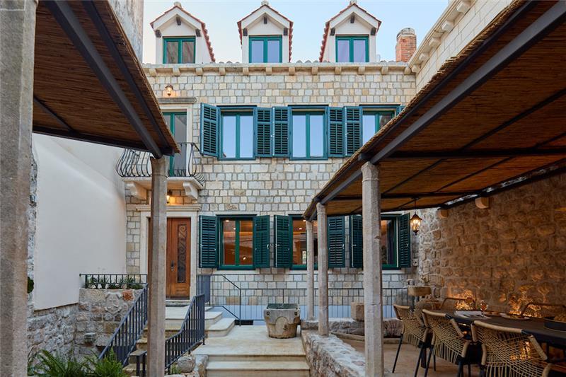 A timber front door at the top of stone steps in the walled courtyard of an old stone villa with green shutters, Dubrovnik Old Town